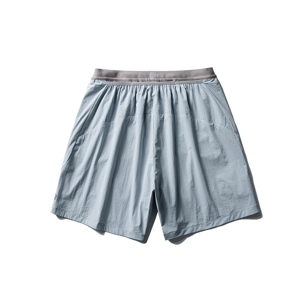 Back view of loose light blue-gray shorts with a gray waistband and curved rear panel seams.