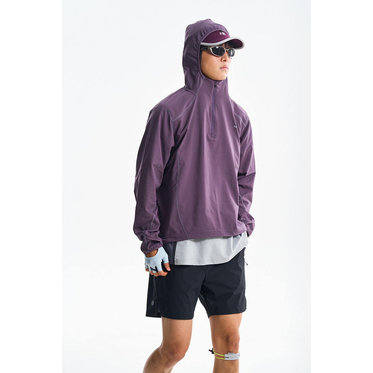 Model wearing a plum-purple hooded pullover with a short front zipper and black shorts against a white background.