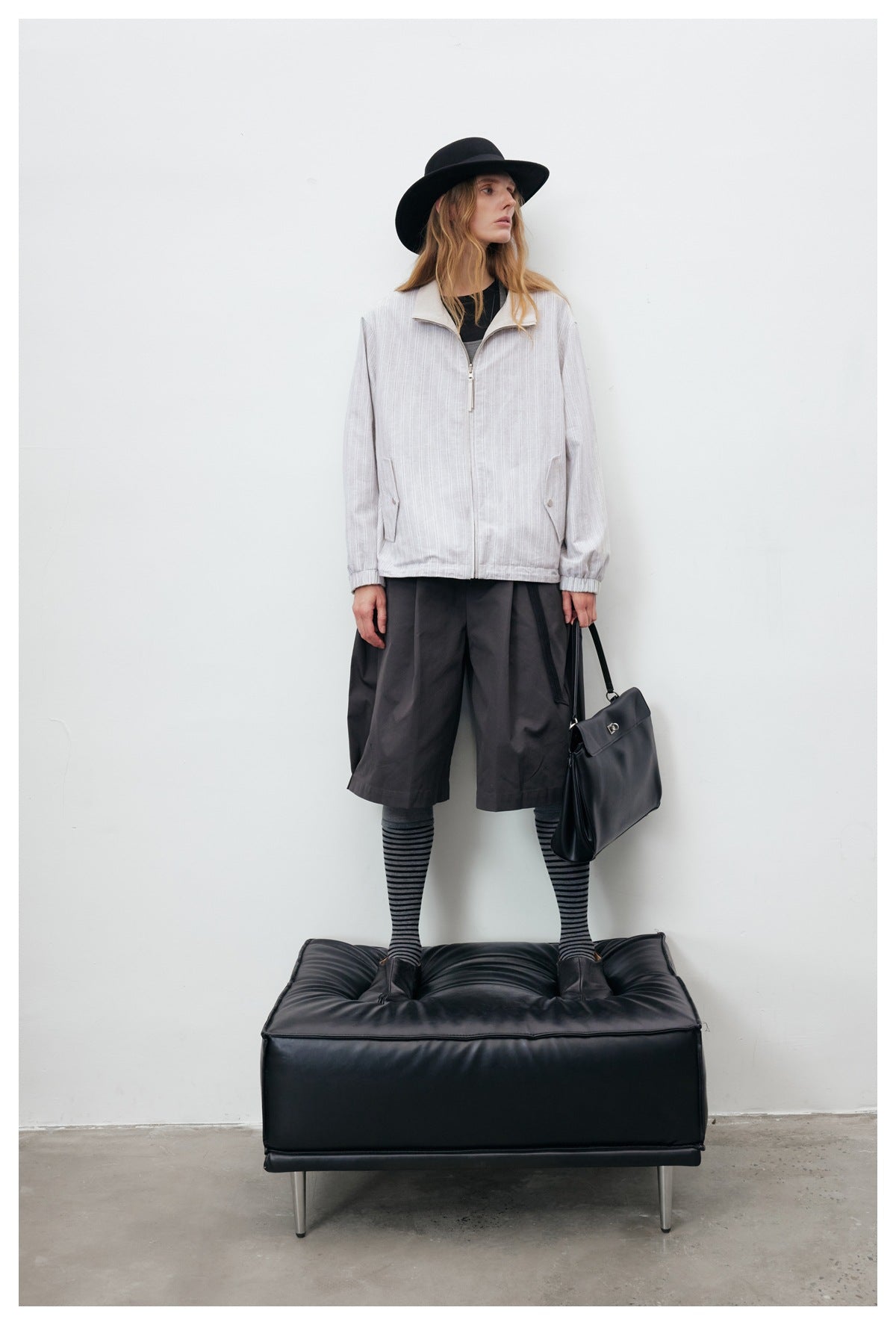 Full-length view of a model wearing a pale gray striped zip jacket with a cream collar and dark shorts.