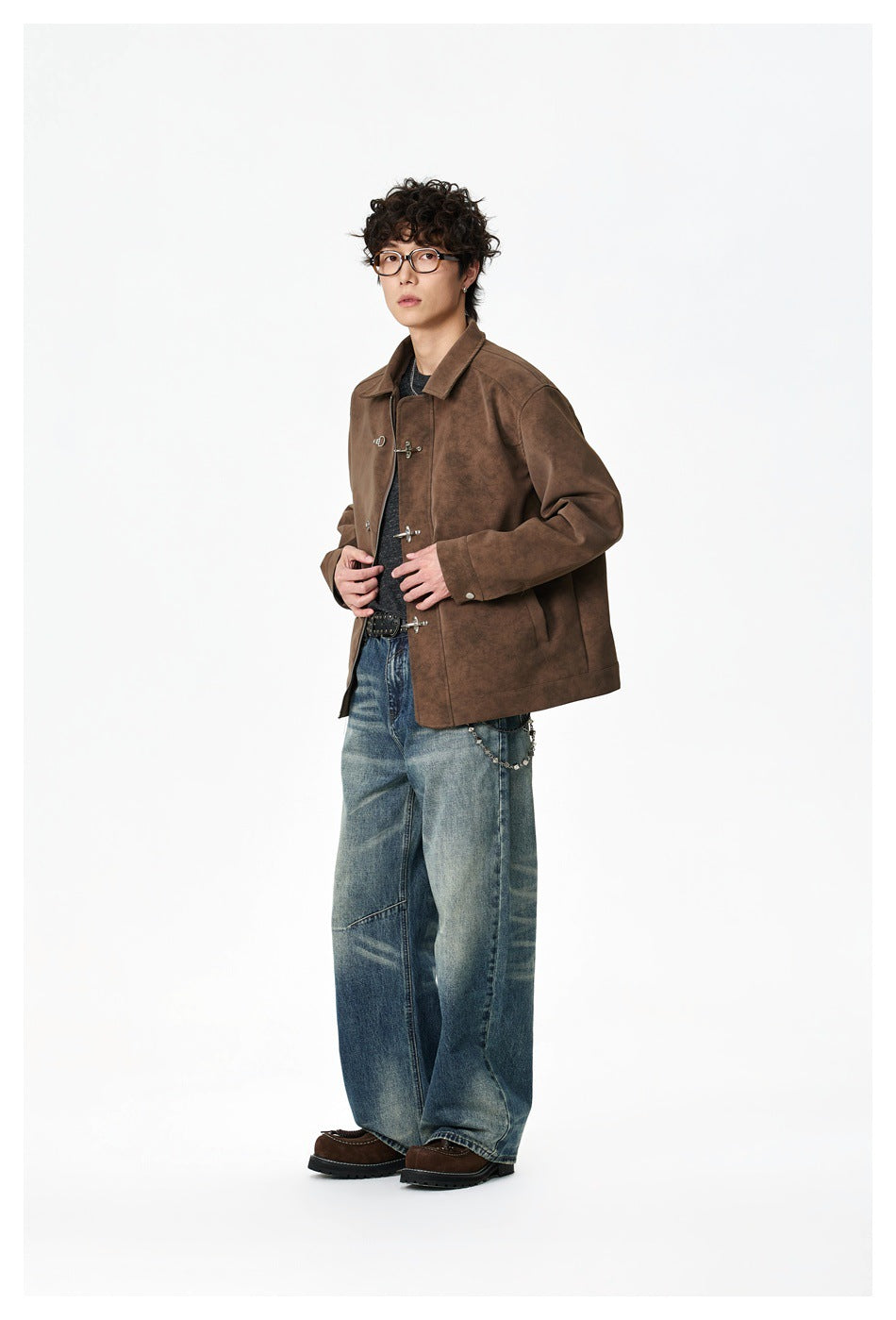 Model wearing a mottled brown jacket with metal clasp closures and loose blue jeans, shown full length.