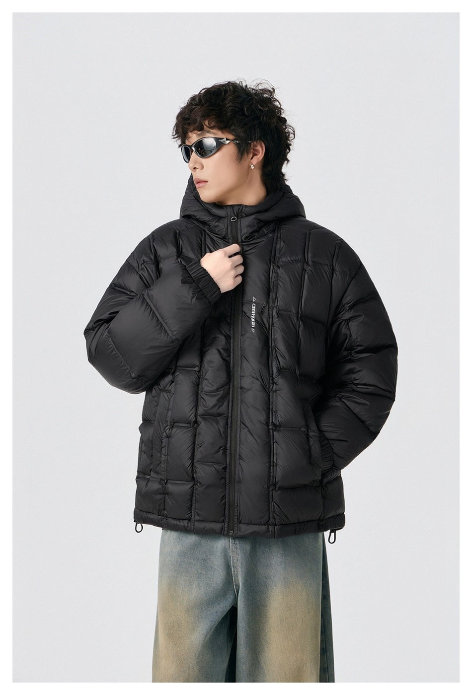 Model in a black hooded puffer jacket, shown from a slight angle with one hand near the collar.