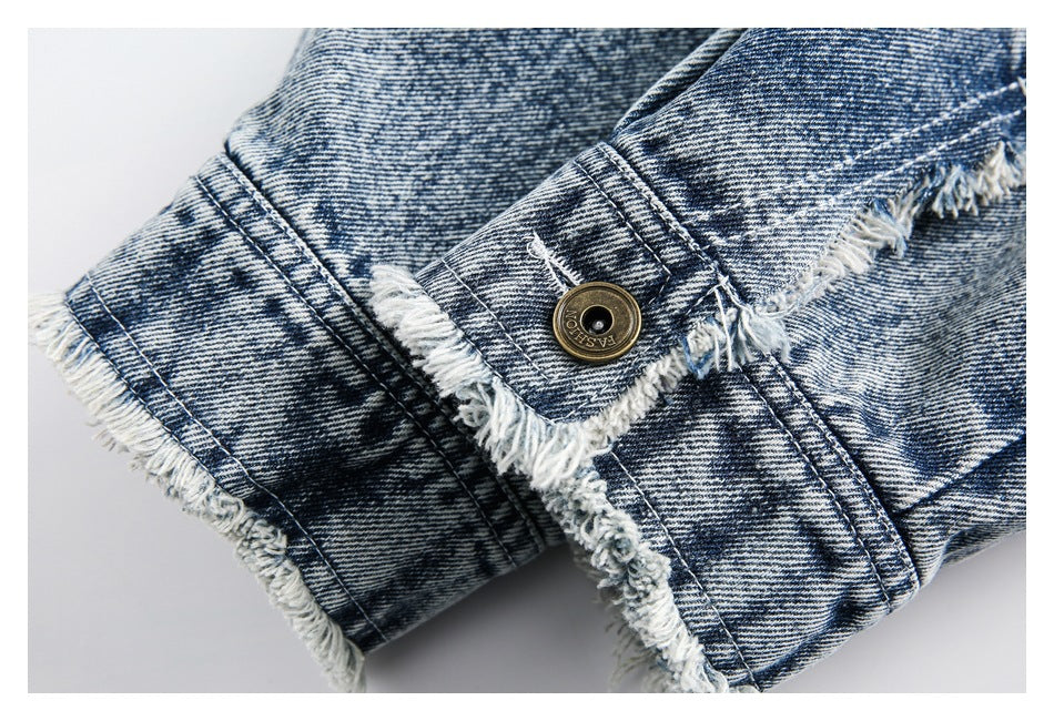 Close-up of a metal button and frayed, overlapping seams on blue acid-wash denim.