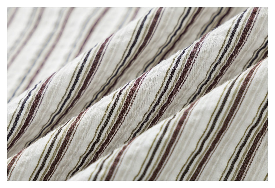 Close-up of softly crinkled white fabric with narrow brown, gray, and olive stripes.