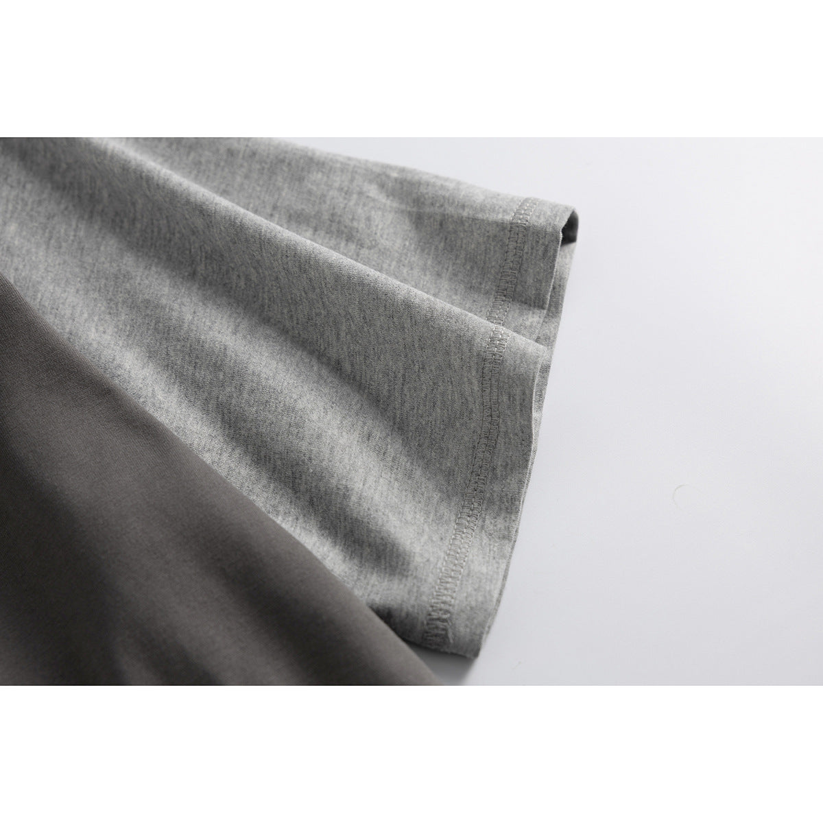 Close-up of a heather-gray T-shirt sleeve and stitched hem against a light background.