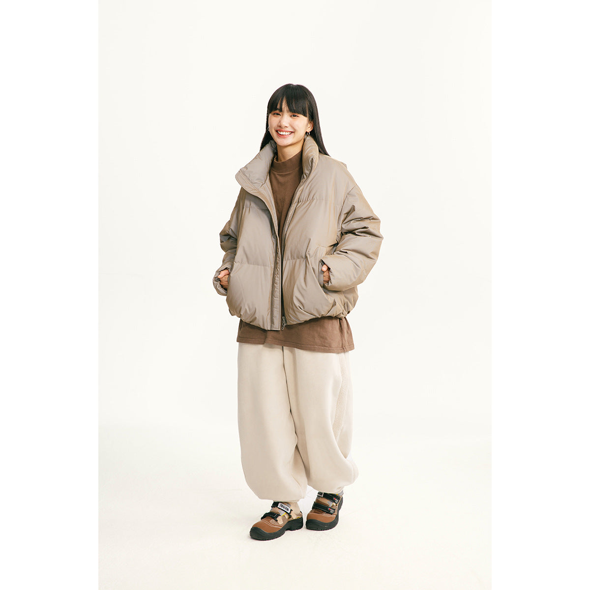 A model wears a taupe puffer jacket with a high collar and front zipper.