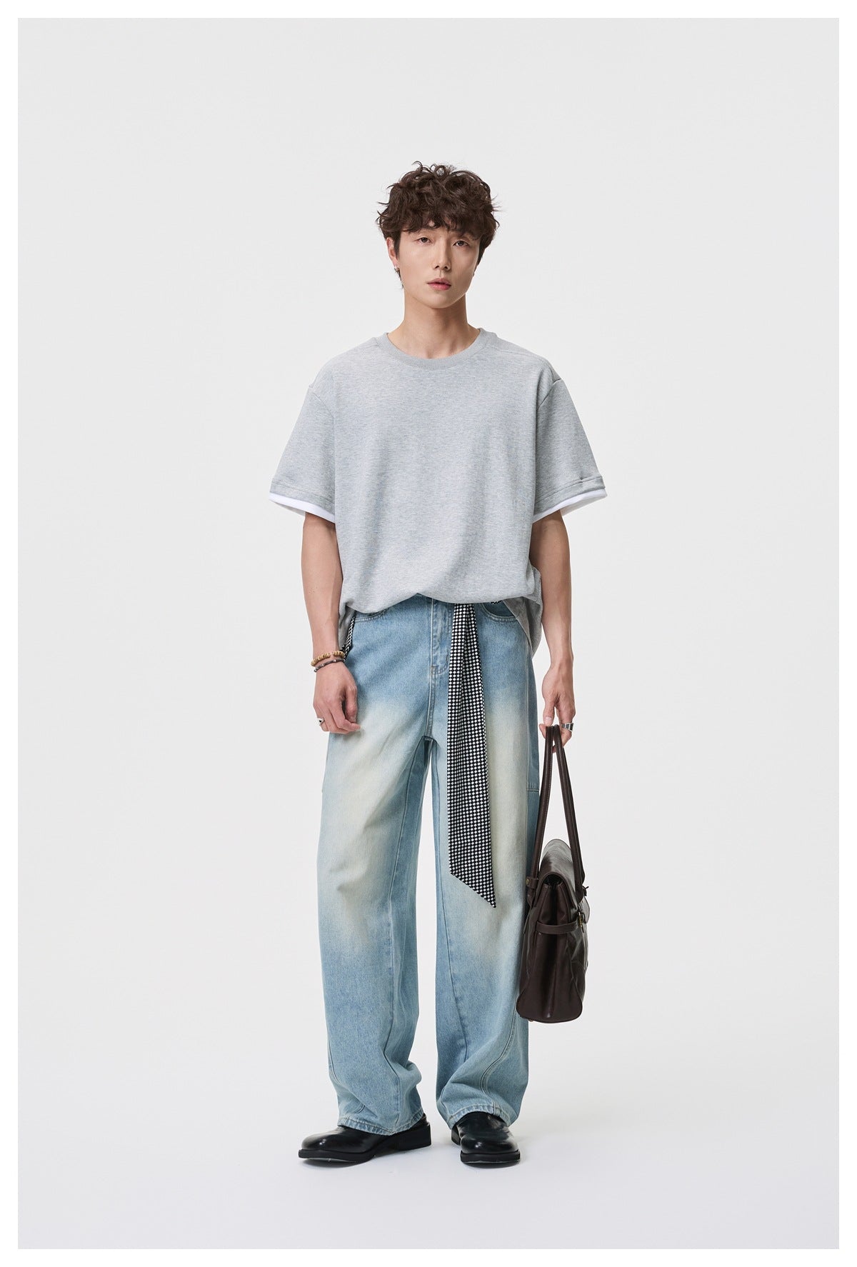 Model wearing an oversized light gray short-sleeve tee with white sleeve trim, styled with loose jeans and a patterned tie.