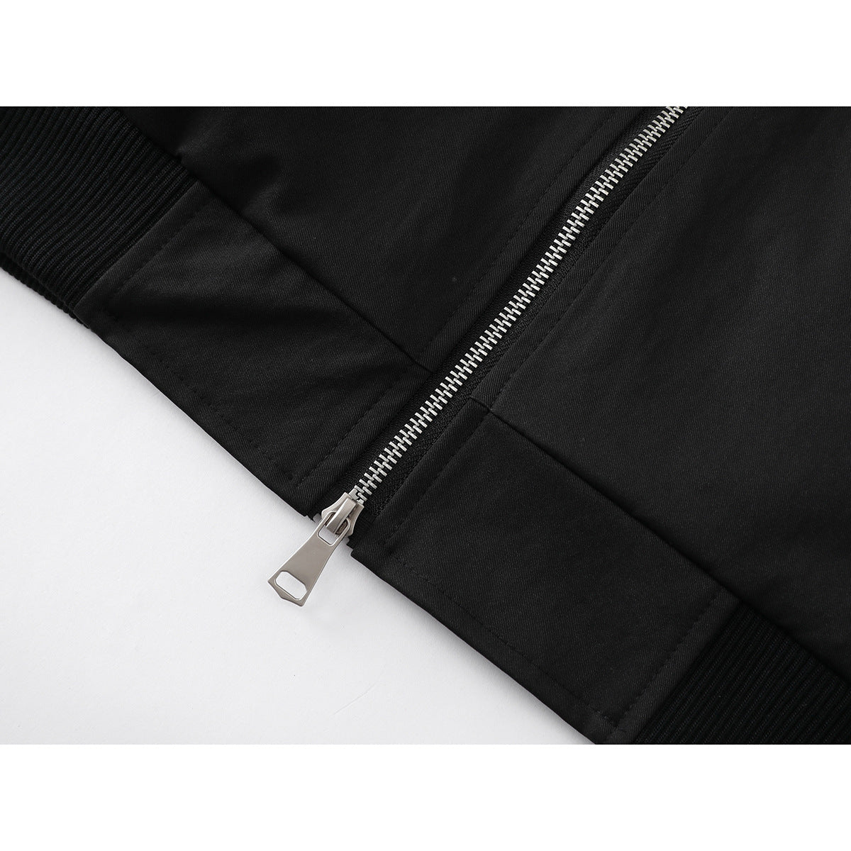 Close-up of a black jacket's silver zipper, front seam, and ribbed hem.