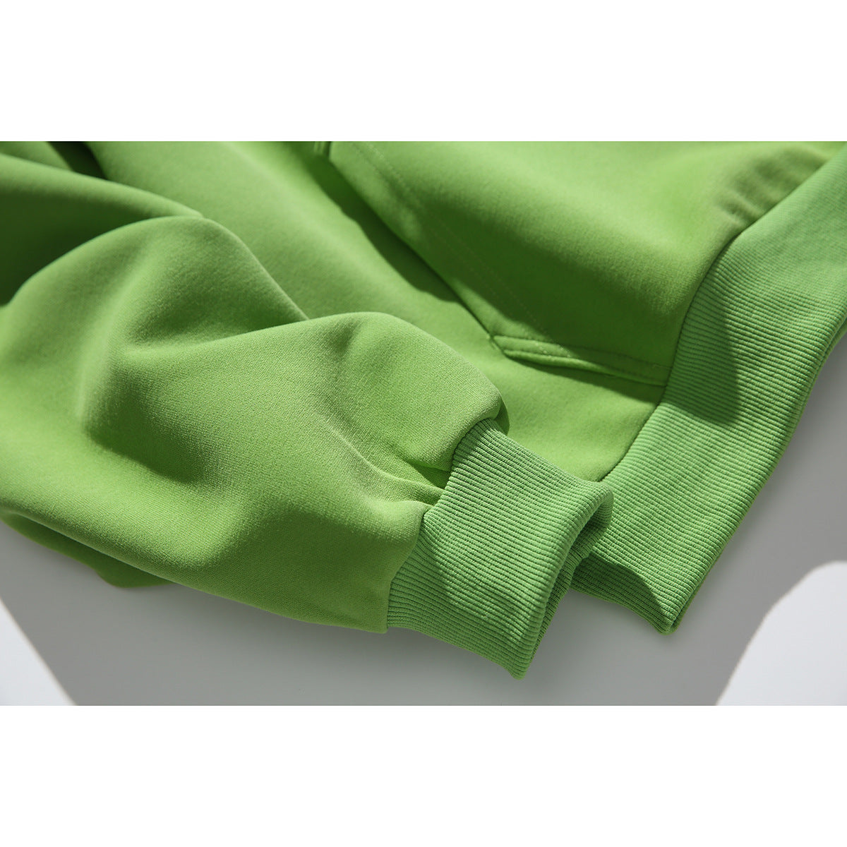 Close-up of a lime-green sweatshirt sleeve and ribbed cuff, with part of the kangaroo pocket visible.