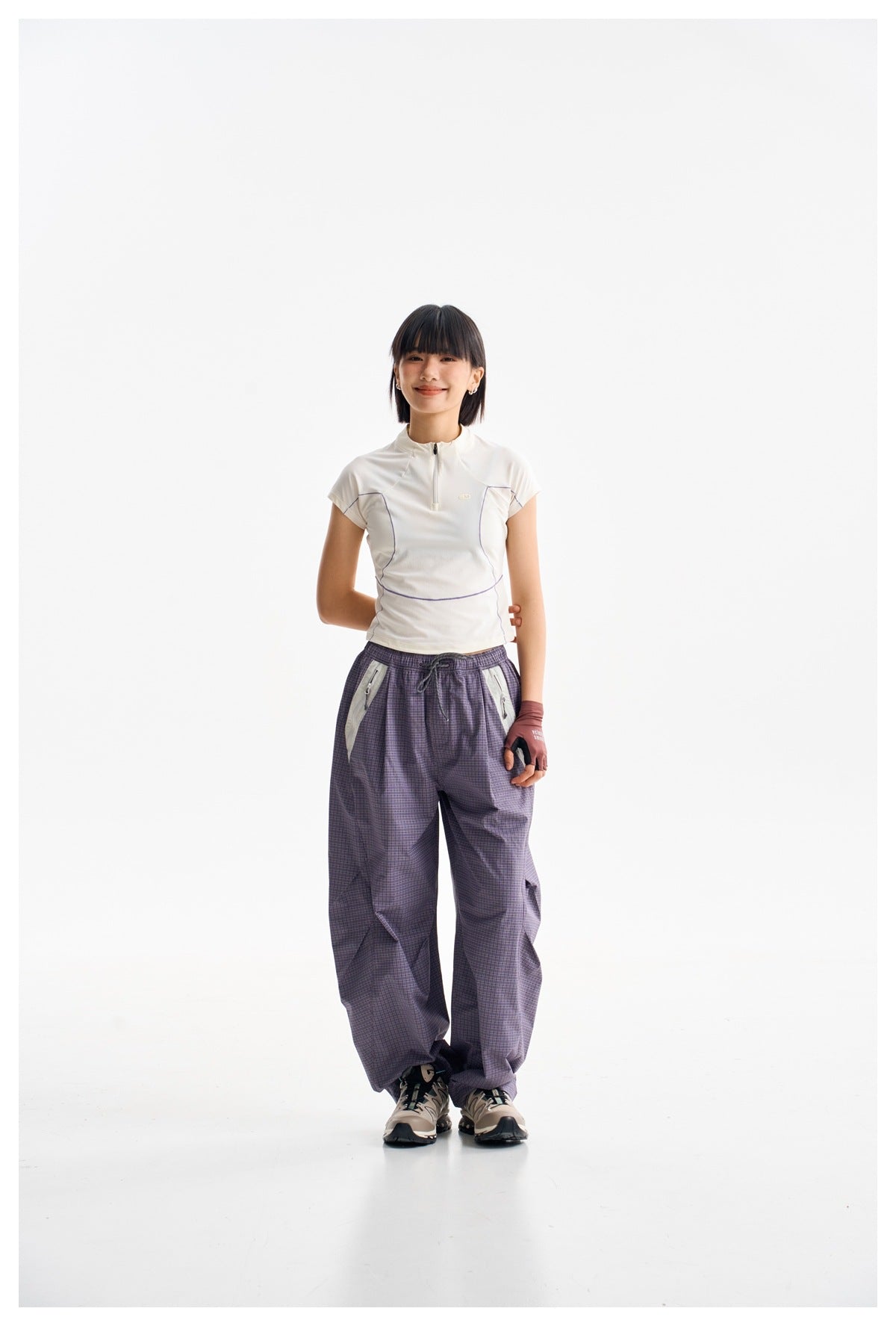 Model wearing a white short-sleeve quarter-zip top with purple seam details and loose purple plaid trousers.