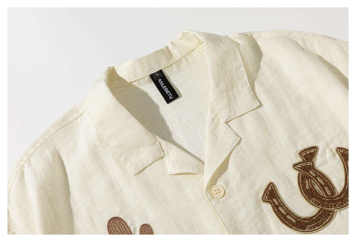 Close-up of an ivory collared shirt with a black neck label and brown embroidered horseshoe motifs.