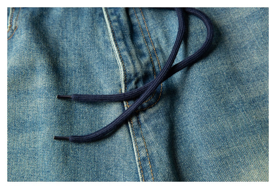 Close-up of dark drawstrings crossing the faded blue denim fabric and orange-stitched seam.