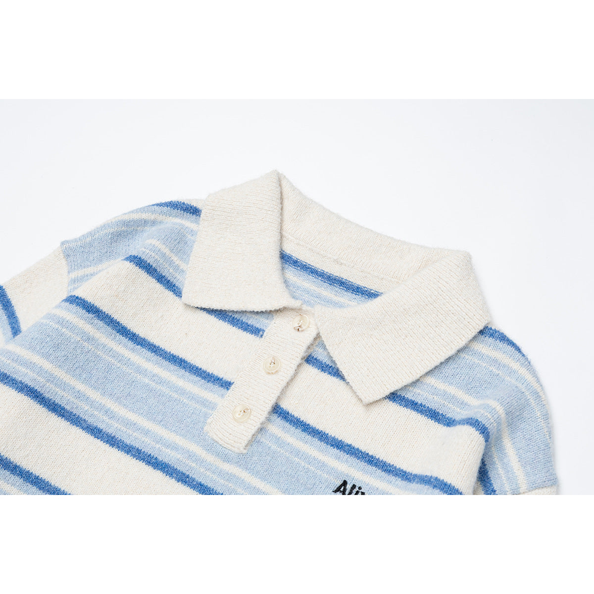 Close-up of an ivory collared knit pullover with blue stripes, three buttons, and partial black chest embroidery.