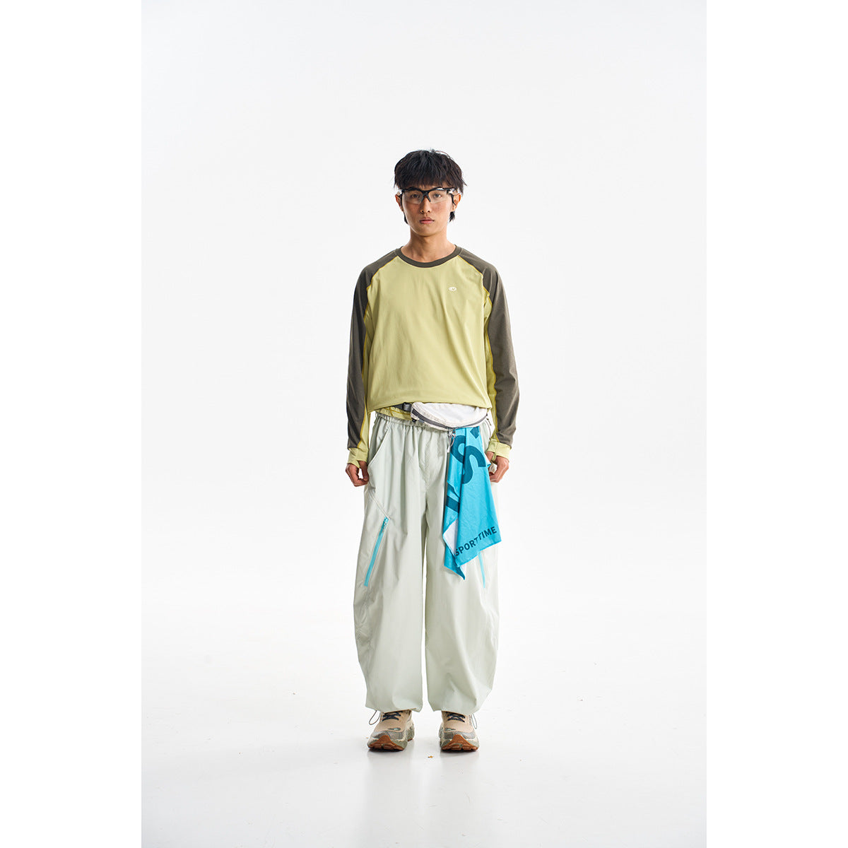 Model wearing a pale yellow long-sleeve top with dark sleeves, loose light trousers, and a blue printed cloth at the waist.