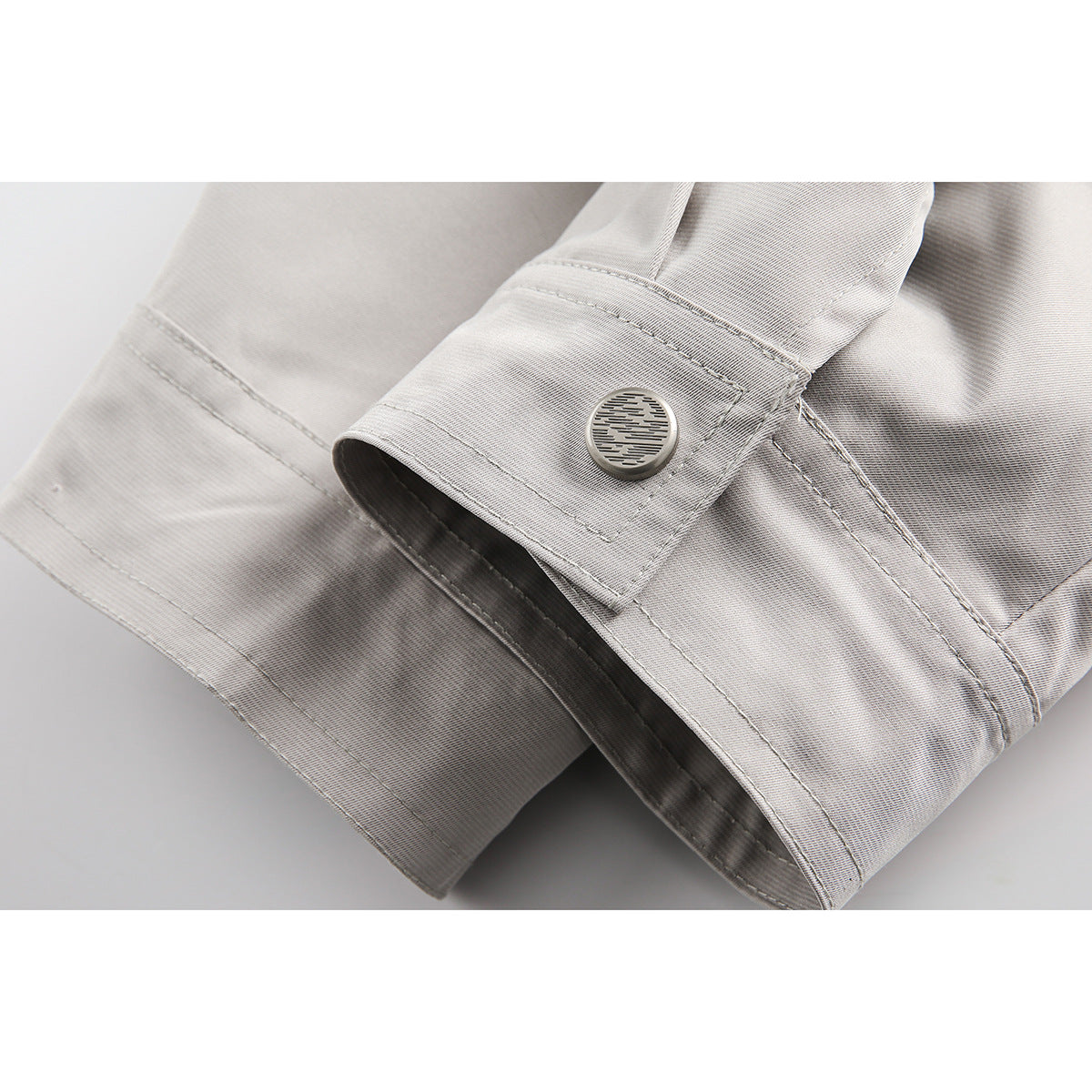 Close-up of a light gray jacket cuff with a round metal button and visible seam stitching.