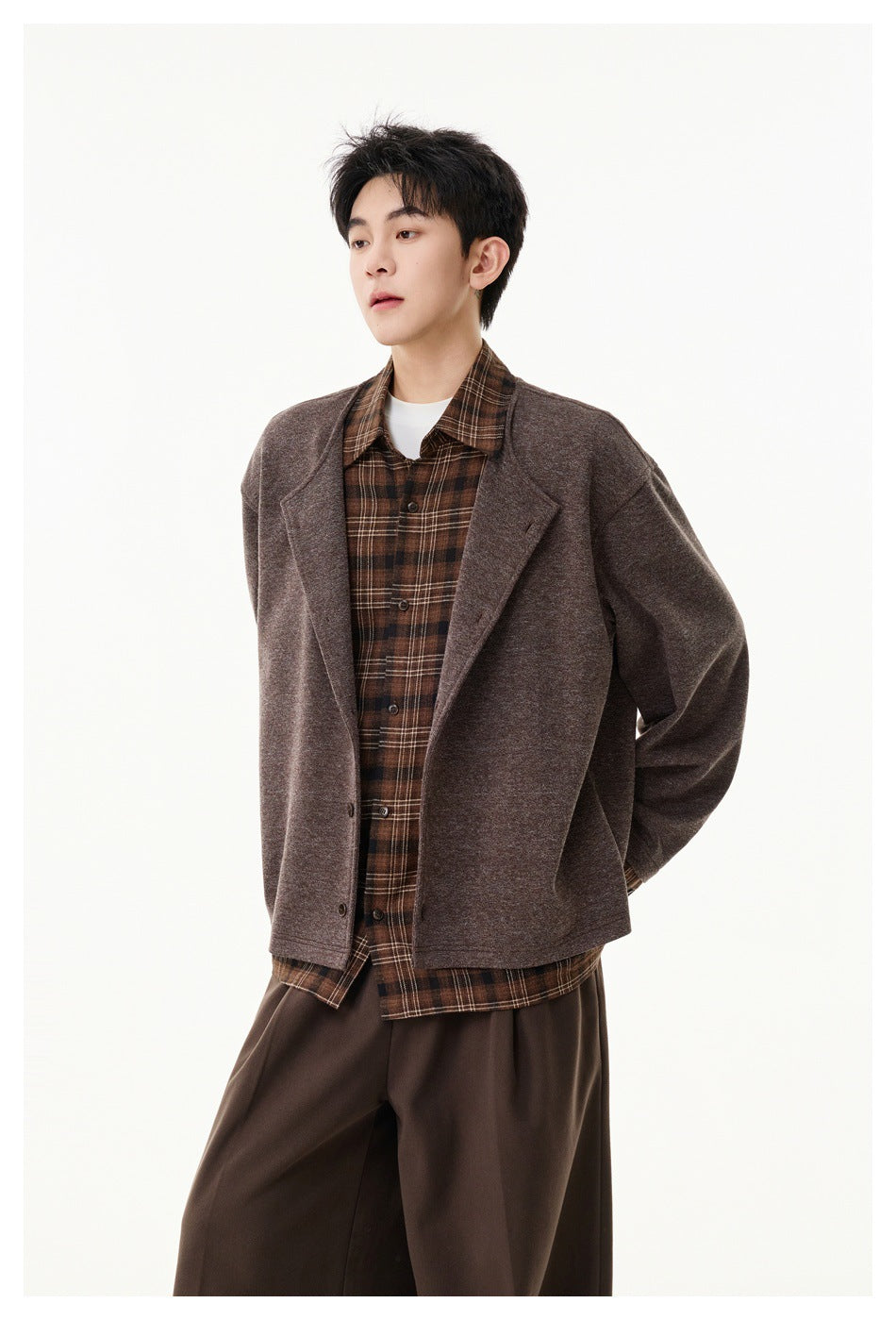 Three-quarter view of a model in a brown jacket with wide lapels, layered over a brown plaid shirt.
