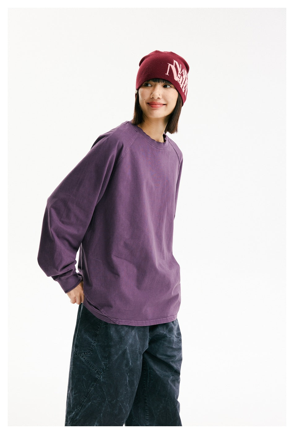 Three-quarter view of a model in an oversized plum-purple long-sleeve shirt and burgundy beanie.