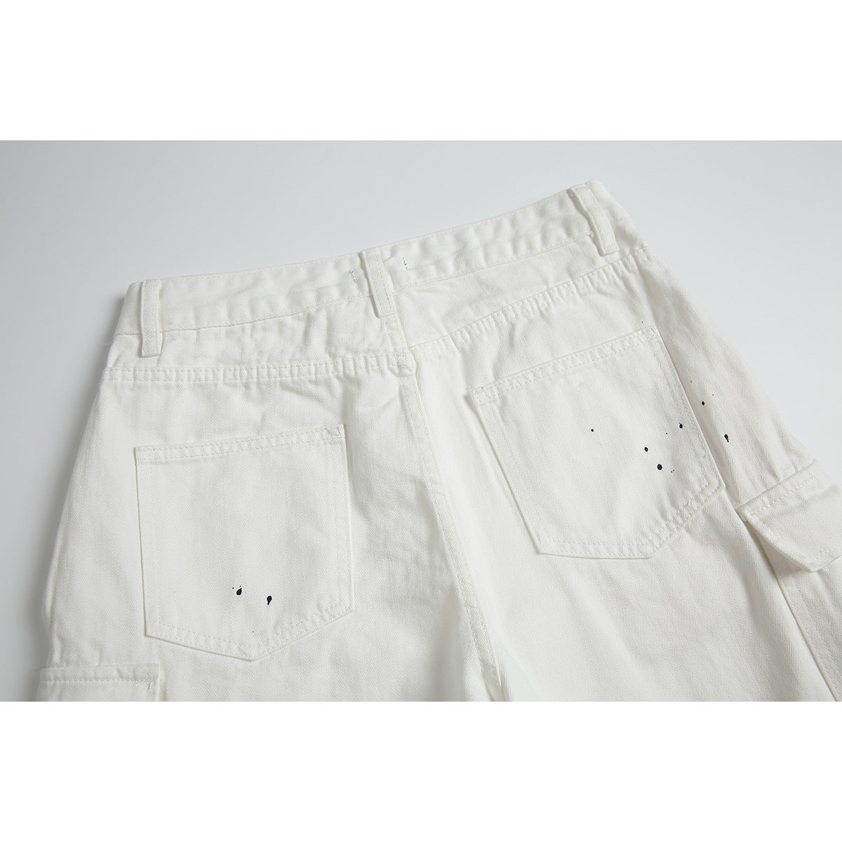 Close view of the back of white pants with two patch pockets and scattered black specks.