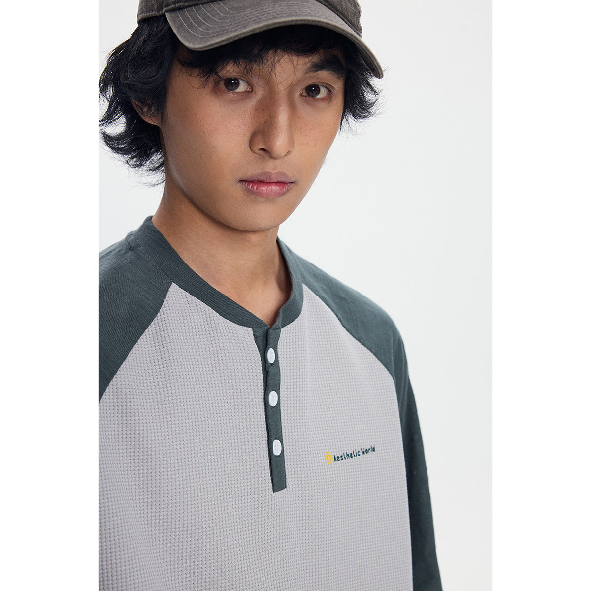 Close-up of a model wearing a light gray waffle-knit henley with dark green raglan sleeves and a three-button placket.