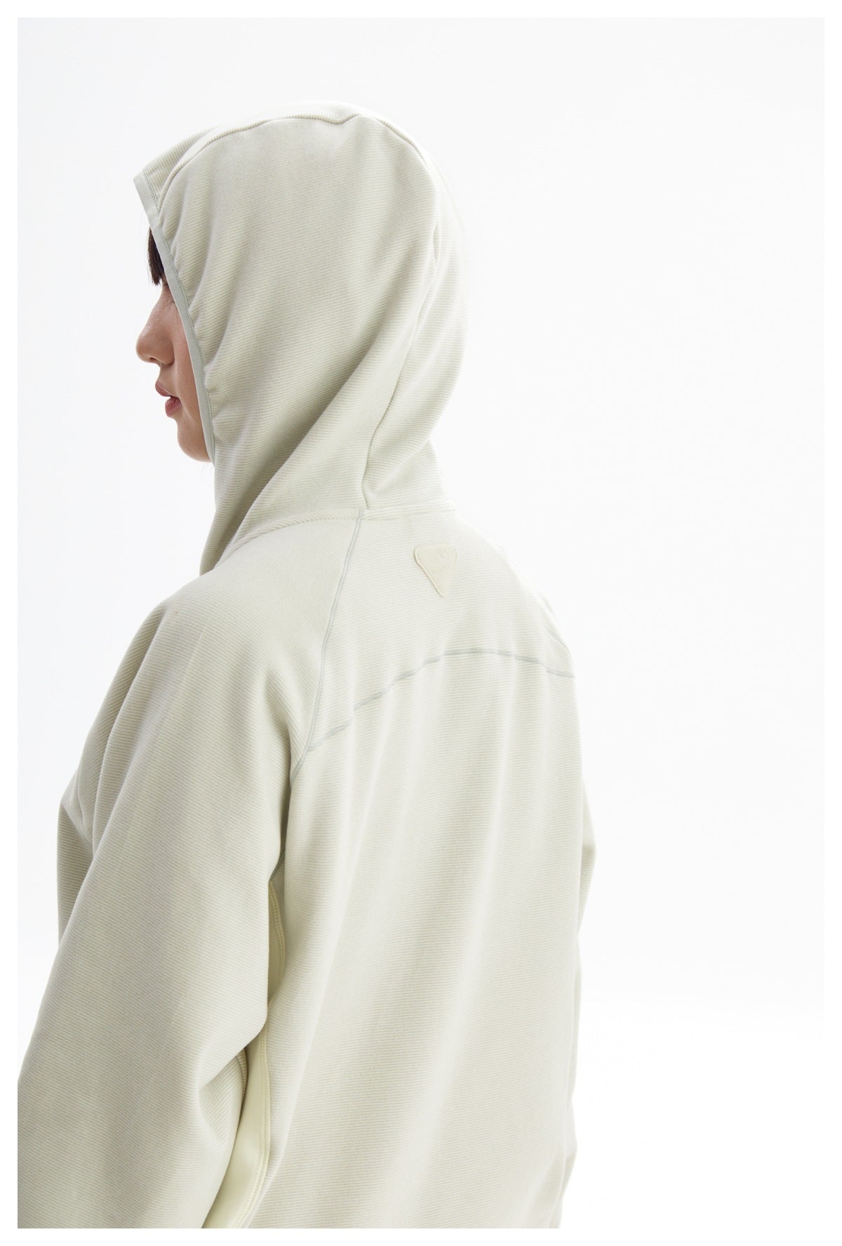 Side and back view of a model wearing an ivory hooded jacket with seam details across the upper back.