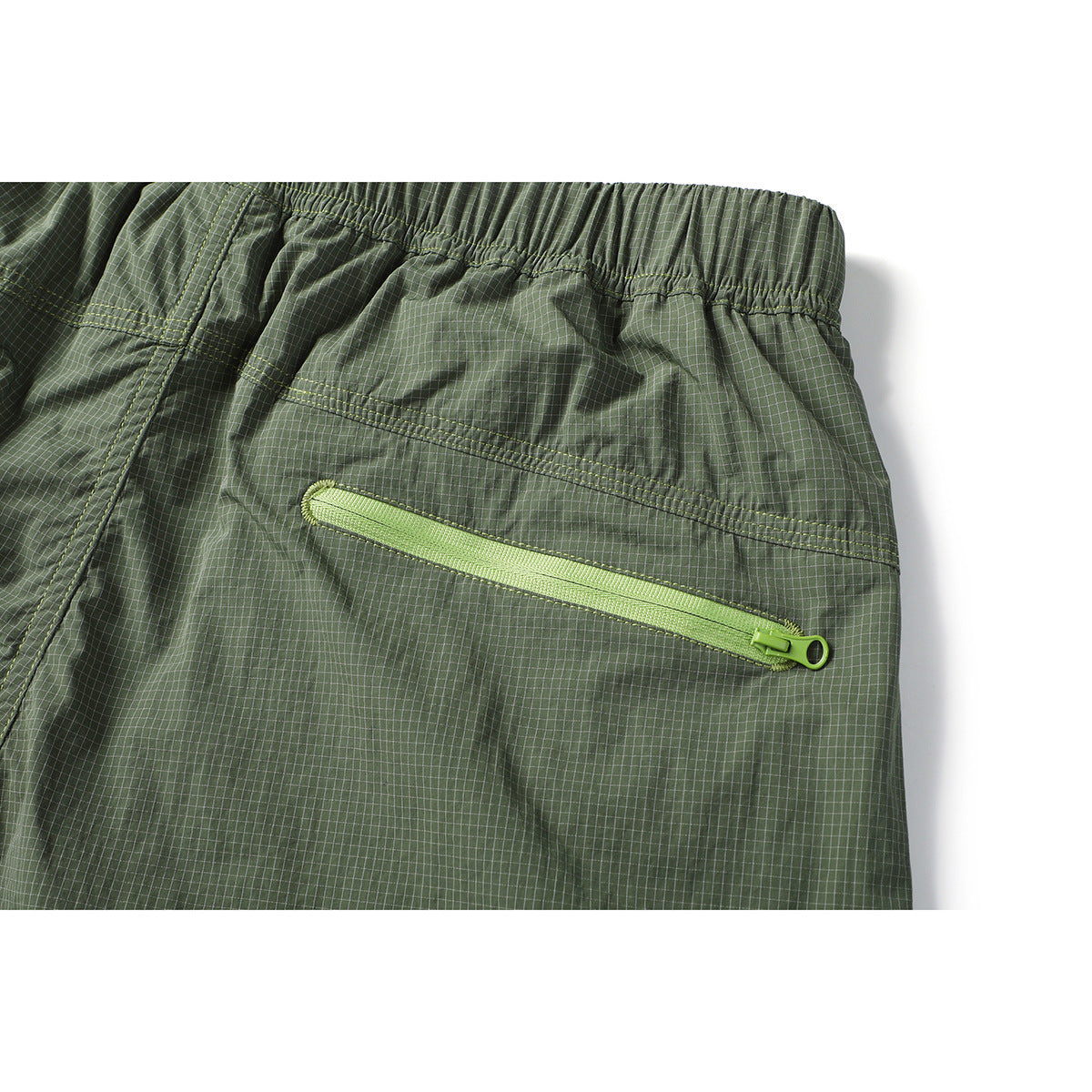 Close-up of olive grid-pattern trousers showing the elastic waistband and a lime horizontal zip pocket on the back.