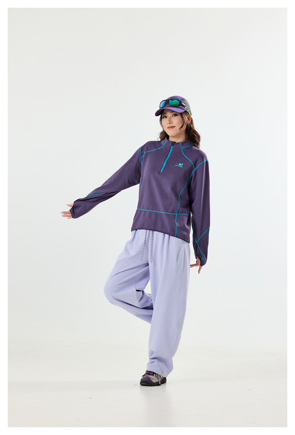 Model wearing a purple quarter-zip top with turquoise seam details and loose lavender pants, shown from the front.