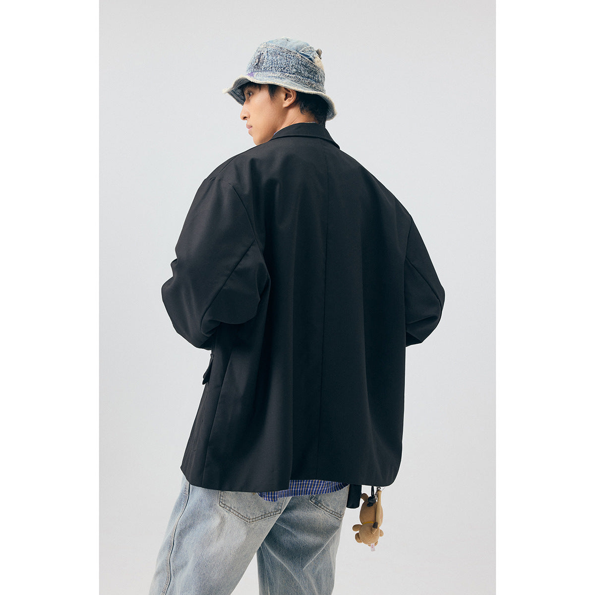 Back view of a model wearing an oversized black blazer, with a blue checked shirt and light jeans.