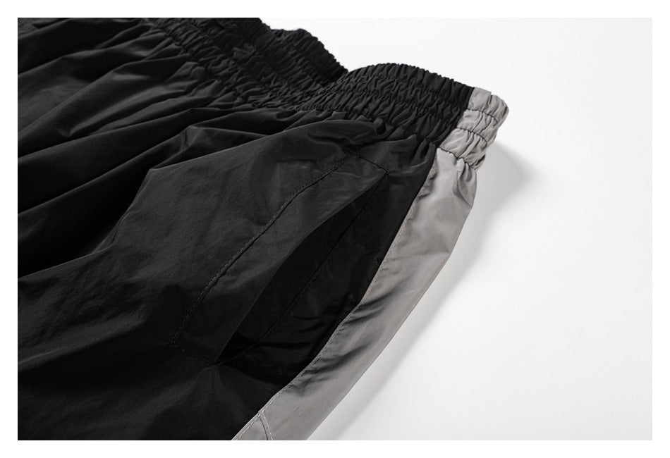 Close-up of black pants with a gathered elastic waistband, pocket seam, and gray side panel.