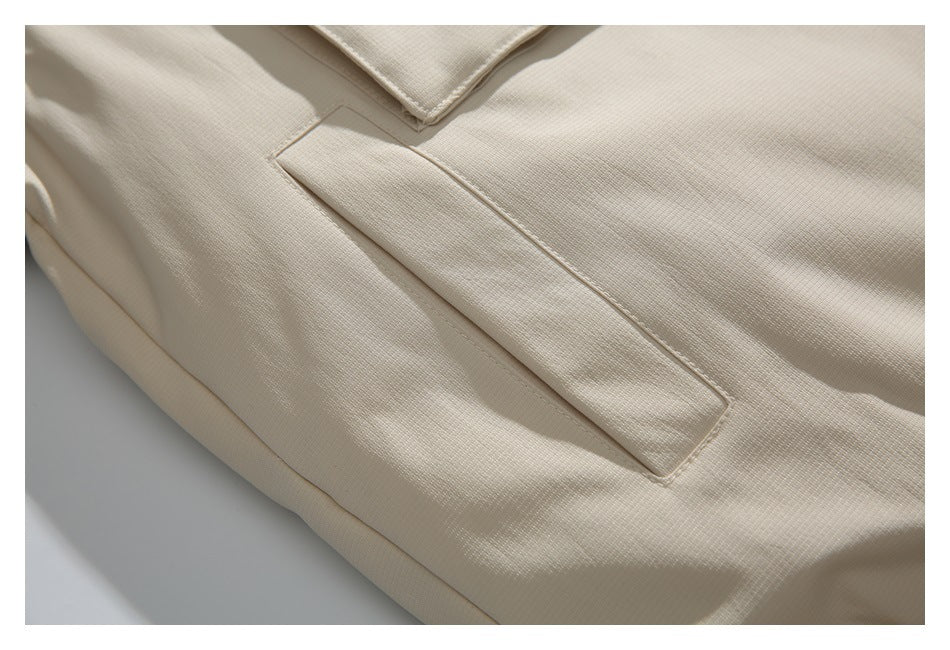 Close-up of a beige jacket's slanted welt pocket and textured fabric.