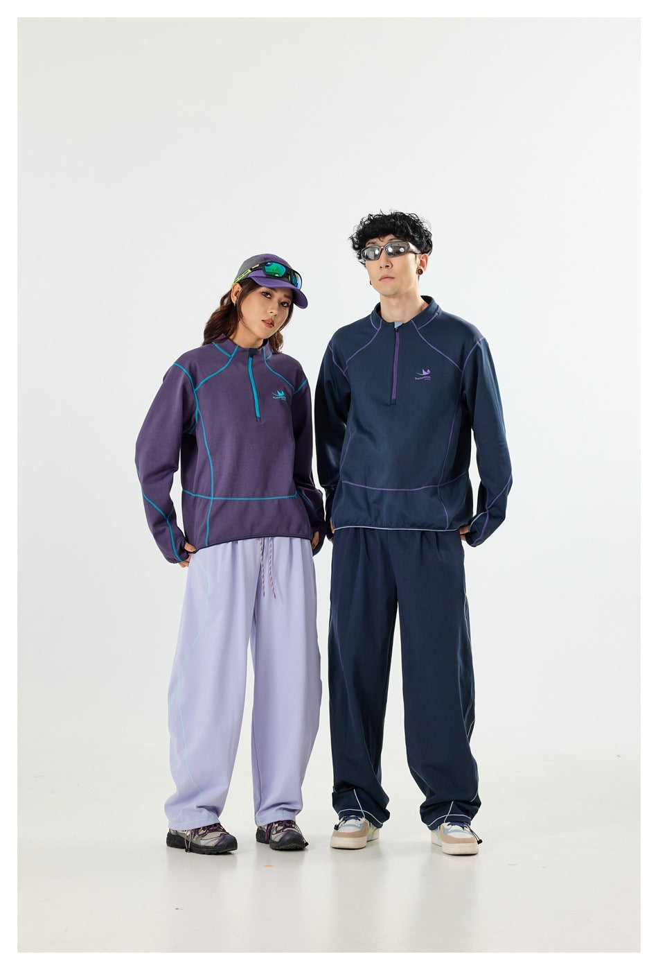 Two models in purple and navy quarter-zip pullovers with contrasting piping and loose matching pants.