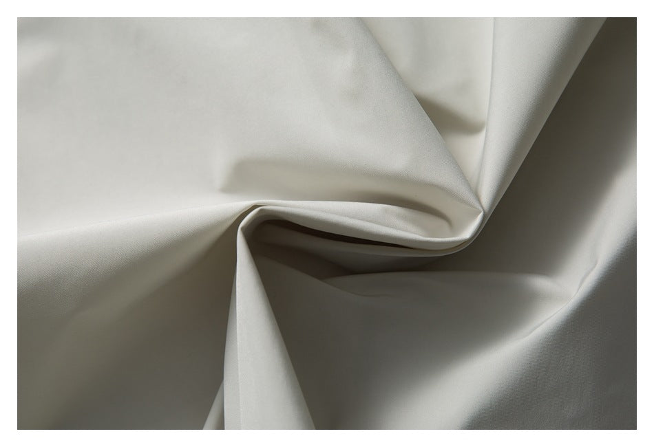 Close-up of smooth off-white fabric draped into soft folds, showing its fine surface texture.