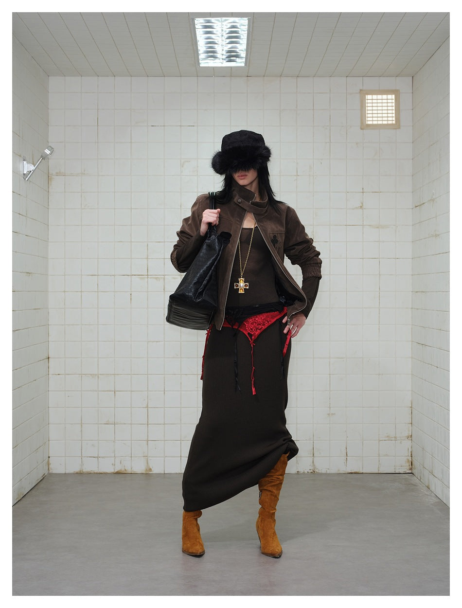 Model wearing the brown zip jacket open over a dark knit dress with a black fur hat and tan boots in a tiled room