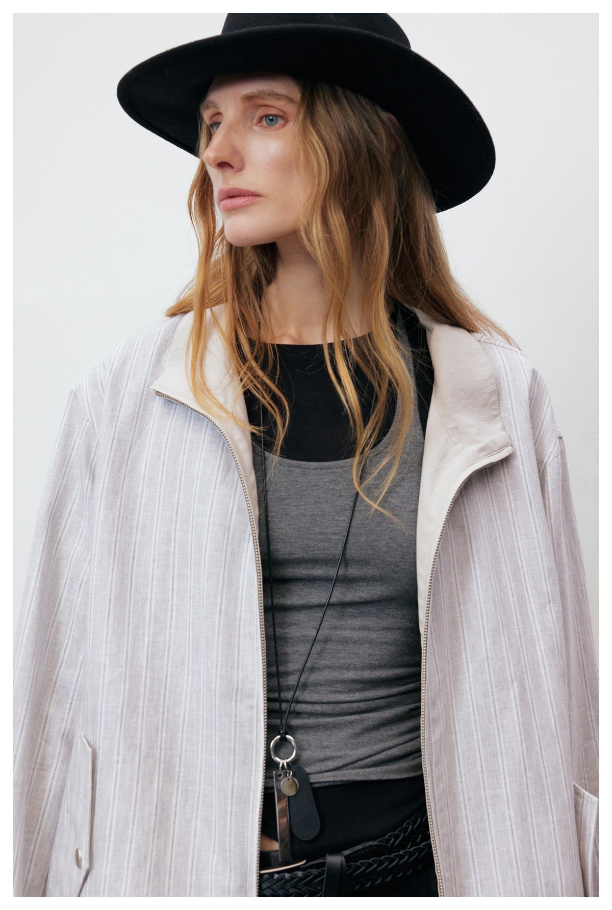 Close view of a pale gray striped jacket with a cream collar and open front zipper, worn by a model.