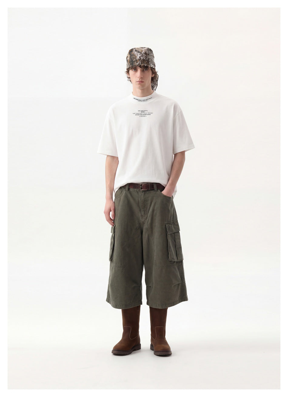Full-length model wearing a white printed T-shirt, olive cargo shorts, brown boots, and a camouflage headscarf.