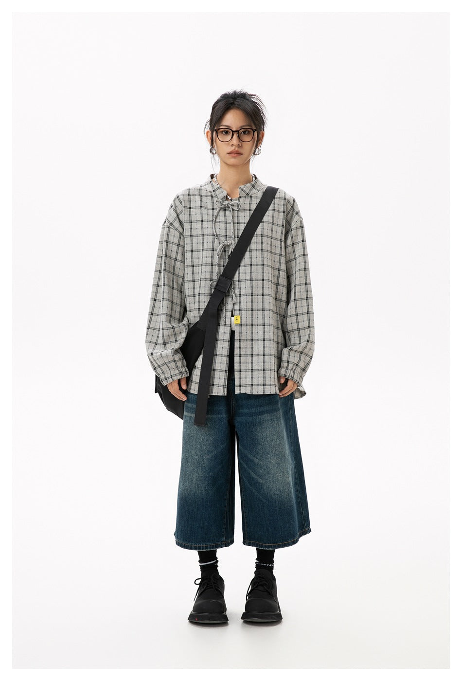 Model wearing a gray plaid, long-sleeve blouse with a stand collar and tie closures, paired with wide-leg denim culottes.