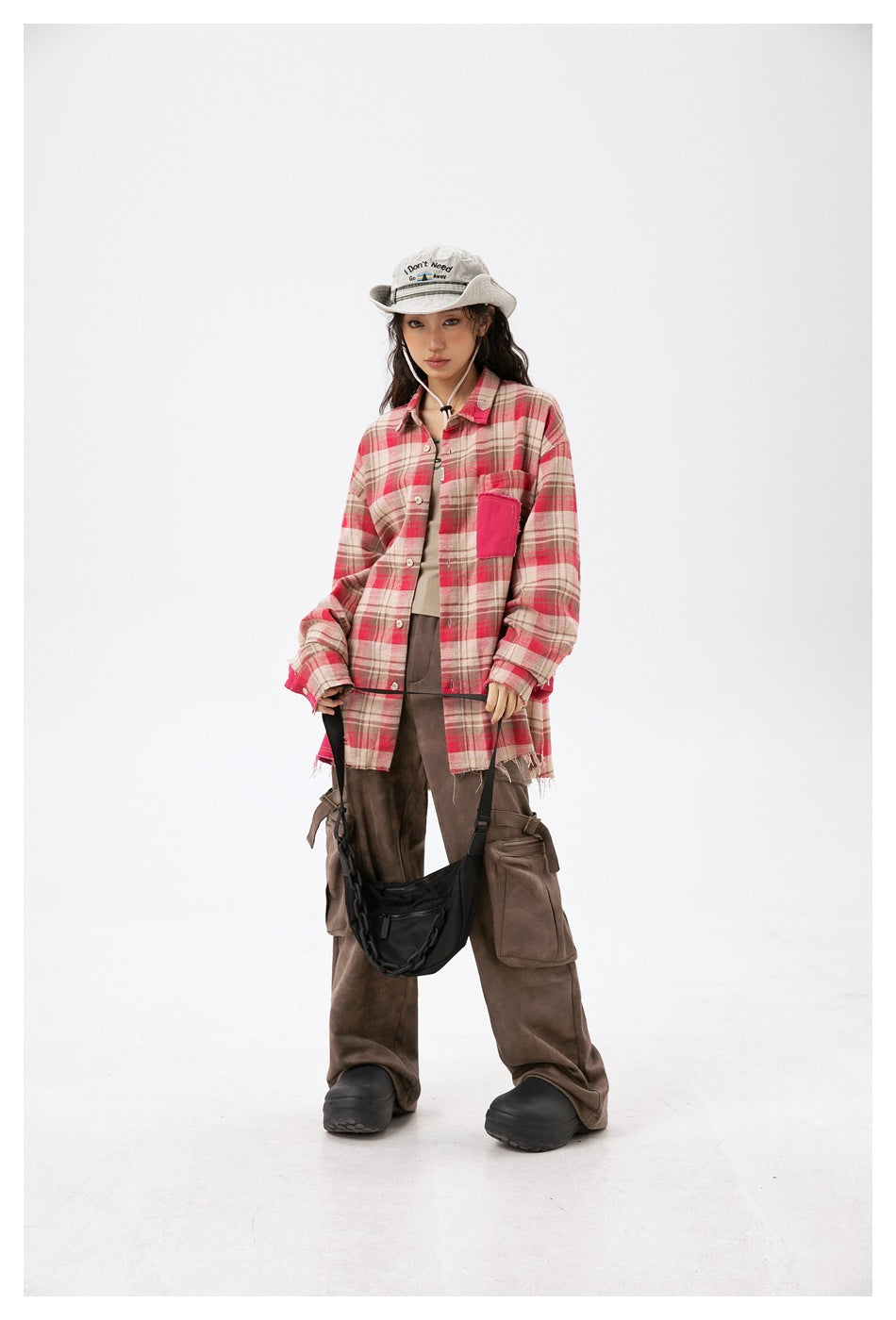 Full-length model wearing an oversized beige and red plaid button-up shirt with a bright pink chest pocket.