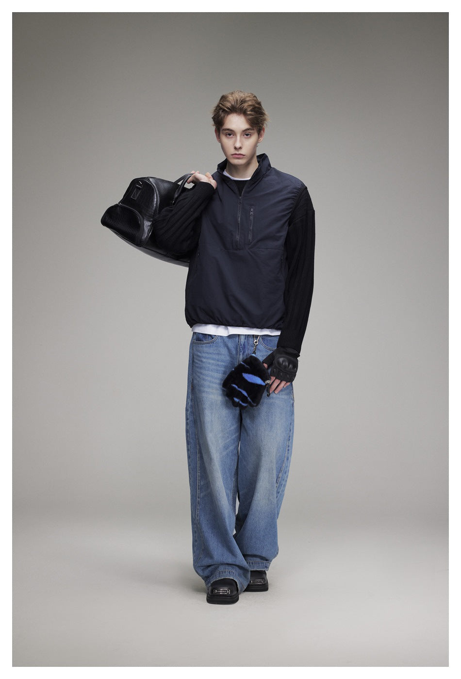 Front view of a model in a navy quarter-zip pullover with black ribbed sleeves and loose blue jeans.