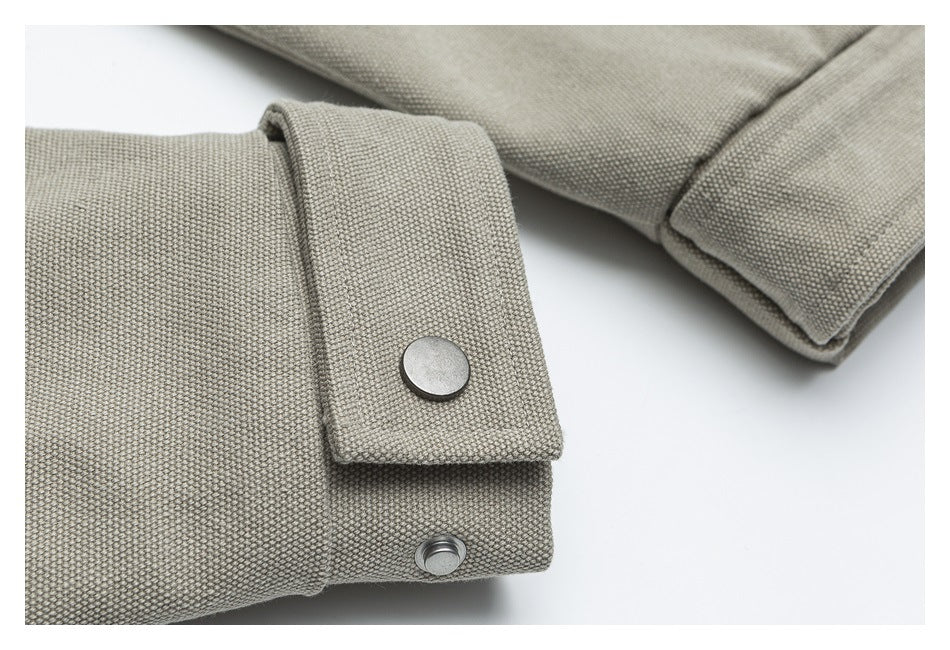Close-up of a beige jacket cuff with a fabric tab and two metal snap fasteners.
