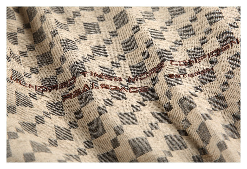Close-up of beige and charcoal geometric-patterned fabric with dark embroidered Latin lettering.