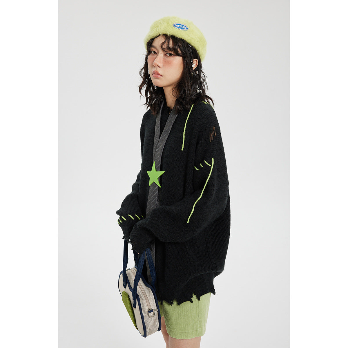 Model wearing an oversized black sweater with lime-green stitched accents and a distressed hem, paired with green shorts.