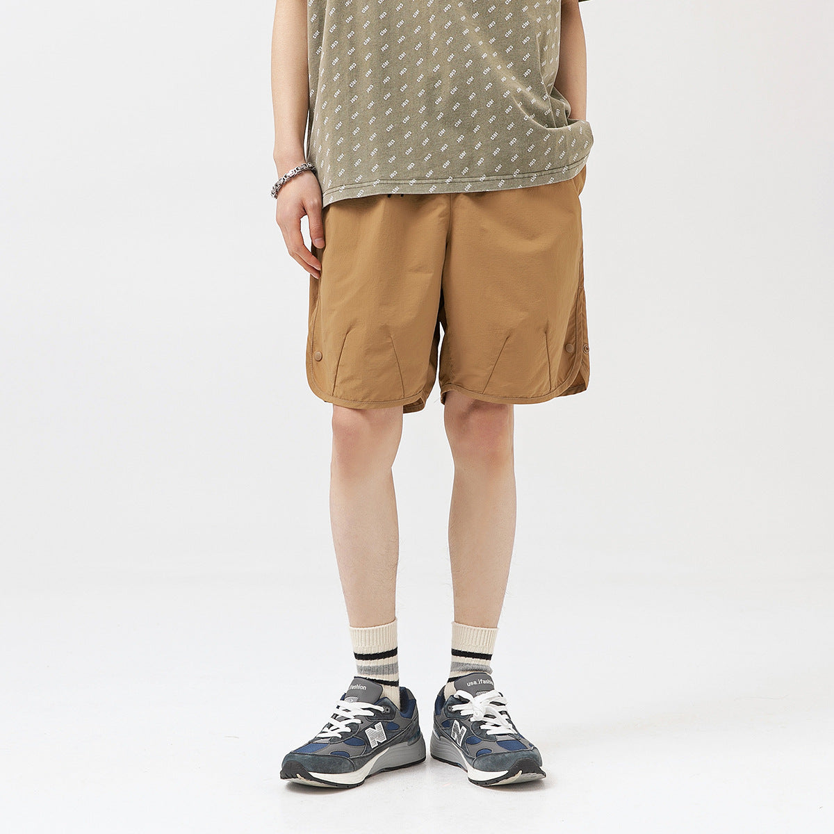 Model wearing loose tan-brown shorts with side snaps, shown from the front.