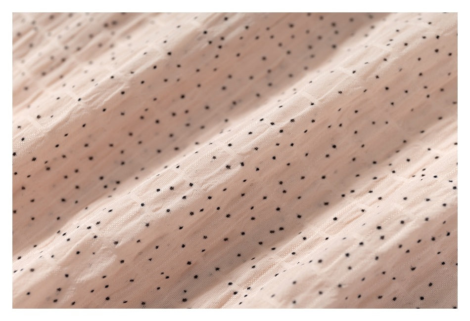Macro view of the pale blush fabric's crinkled texture and scattered tiny black dots.