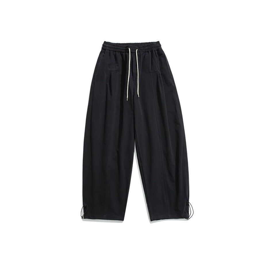 Black wide-leg drawstring pants with elastic waistband, front pleats and toggle hem cinches, flat lay on white