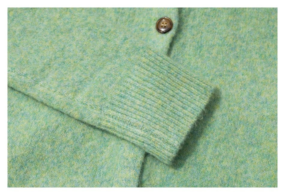 Close-up of a ribbed sleeve cuff and brown button on mottled mint-green knitwear.