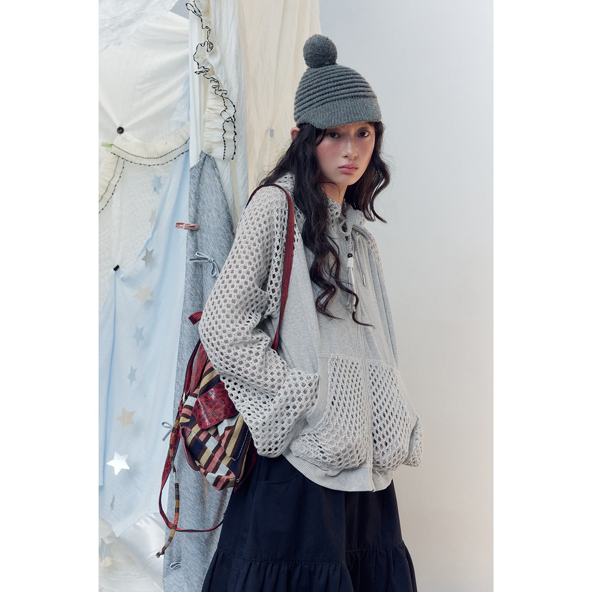 Close view of a model in a light gray zip hoodie with mesh sleeves and pockets, paired with a navy skirt.