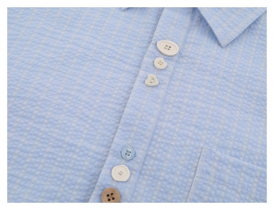 Close-up of a light blue subtly checked shirt front, showing the collar, chest pocket edge, and assorted buttons.