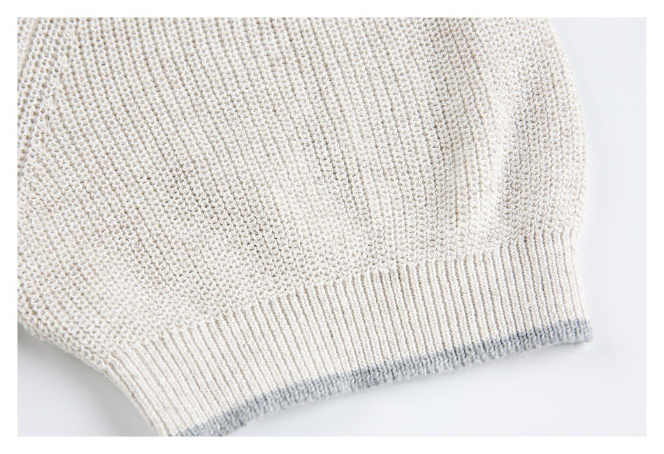 Close-up of an ivory knit sweater sleeve ending in a ribbed cuff with a subtle gray edge.