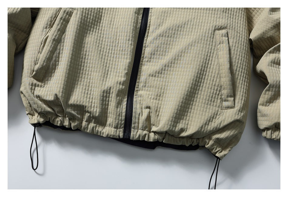Close-up of the light khaki jacket's slanted pockets, quilted fabric, gathered hem, and drawcords.