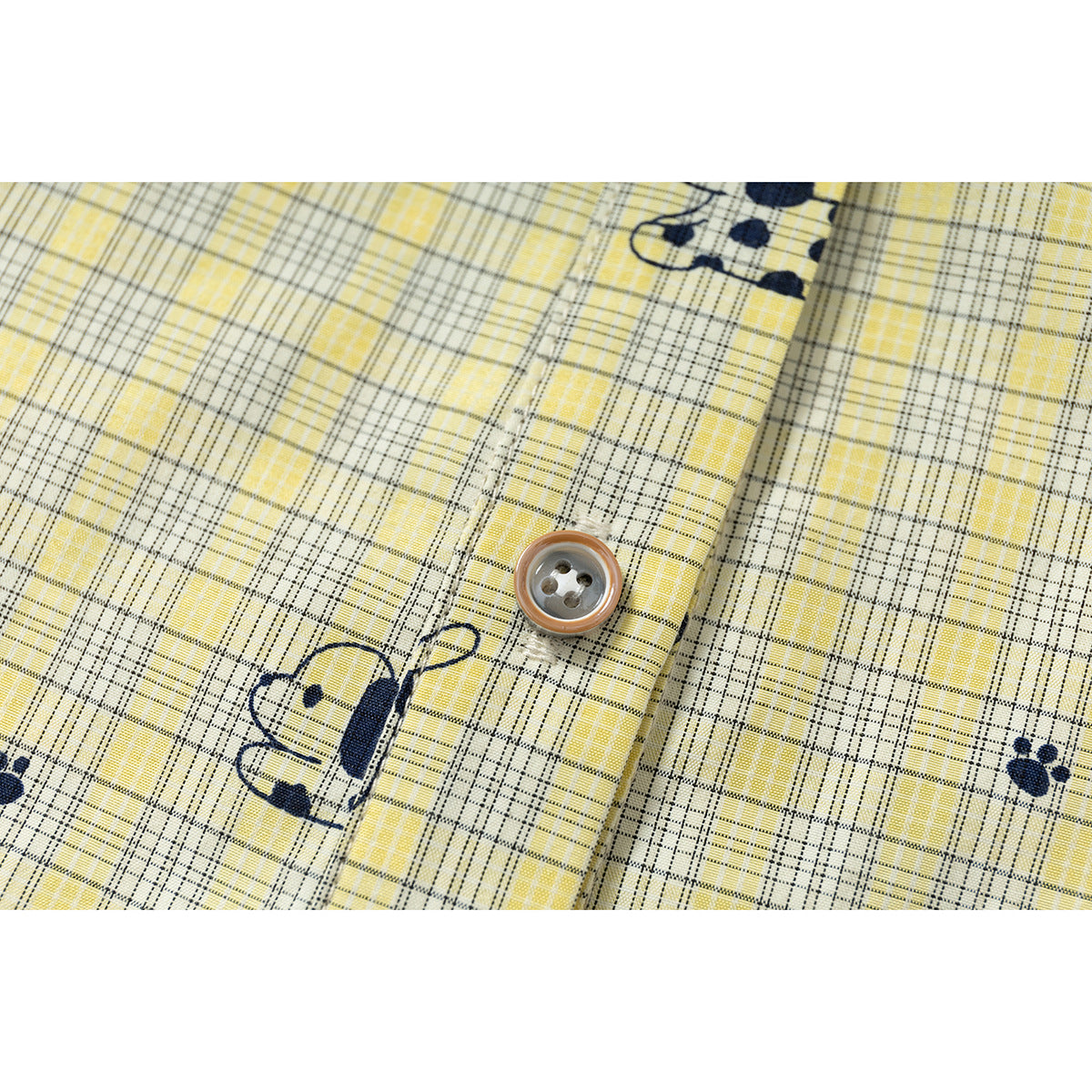 Close-up of a brown-rimmed button and navy animal print on yellow plaid shirt fabric.