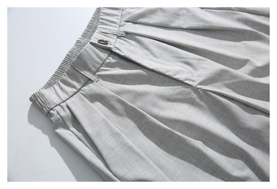 Angled close-up of light gray trousers showing the elasticized waistband, belt loop, button, and front pleats.