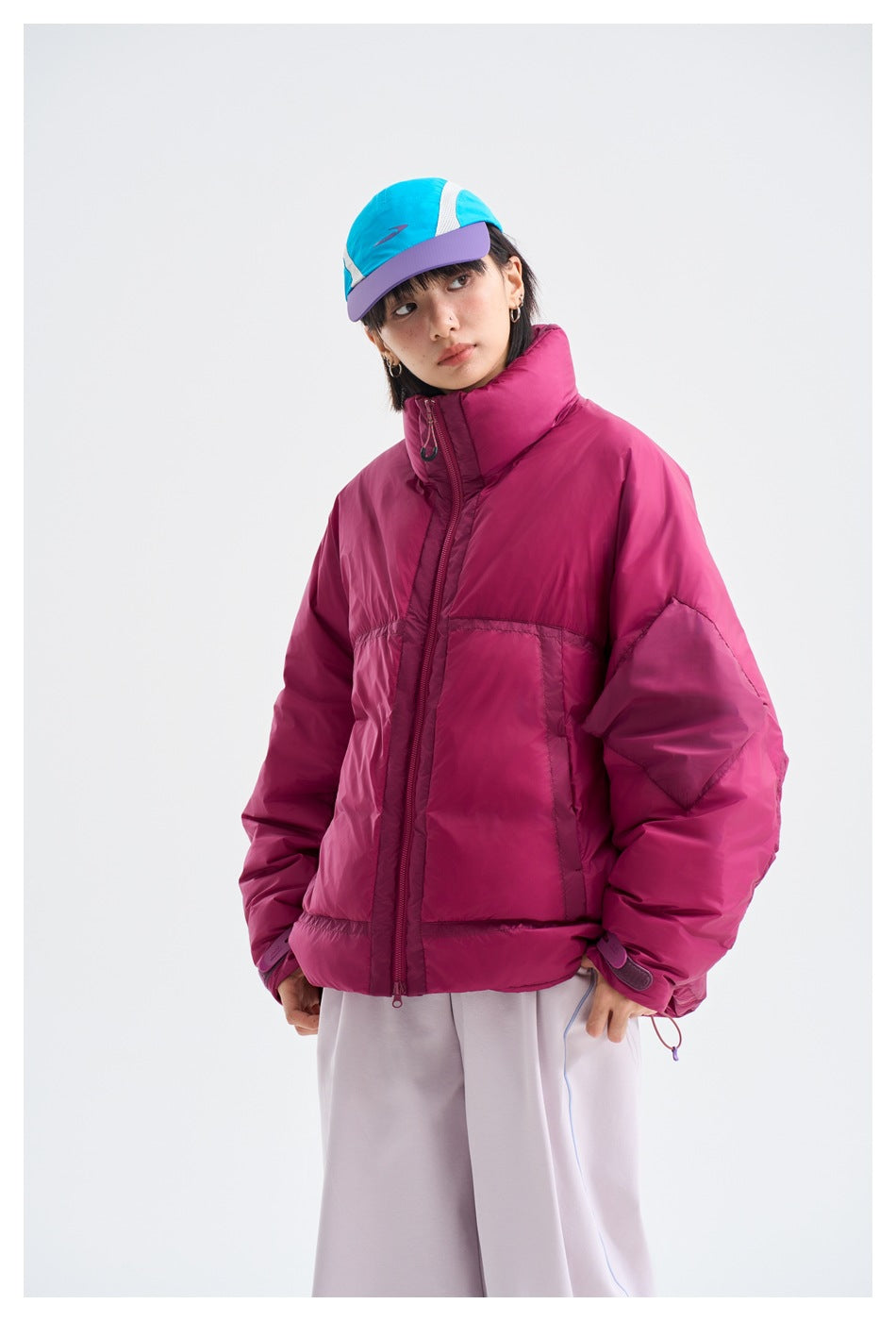 Three-quarter view highlighting the magenta puffer jacket's high collar, oversized sleeves, zipper, and pocket details.
